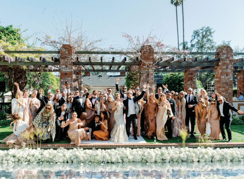 A wedding party and guests, all dressed in clothing that corresponds with a neutral color palette, pose for a group photo 