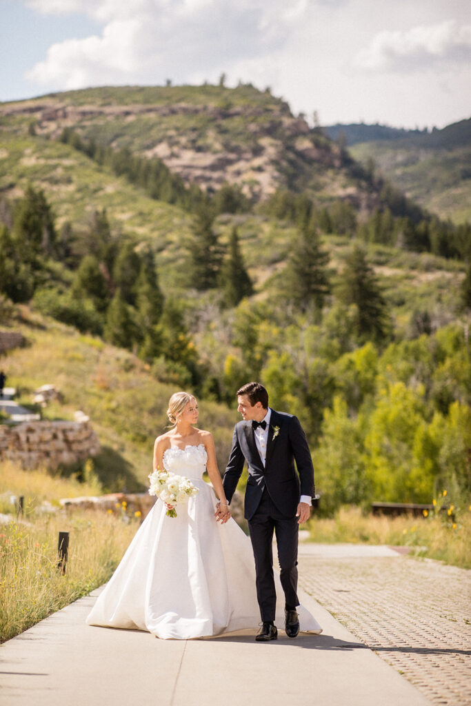 A bride and groom in the Wasatch Mountains hold hands on a sunny day