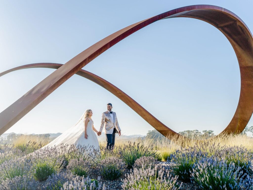 A bride and groom hold hands beneath the Infinity Sculpture at Stanly Ranch