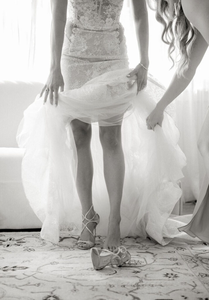A member of a bridal party assists the bride with shoe fitting for a chosen wedding dress