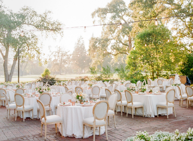 An outdoor reception with soft lighting, elegant white linens, and lush greenery