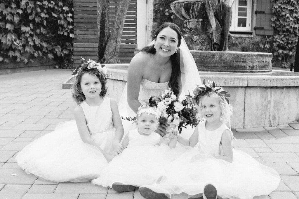 A bride poses with three children outdoors, sitting on the ground in a black-and-white photo