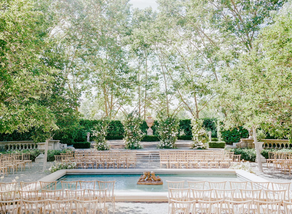A romantic garden ceremony setup at Beaulieu Garden with wooden chairs, floral archways, and a tranquil fountain framed by lush greenery and classical stonework