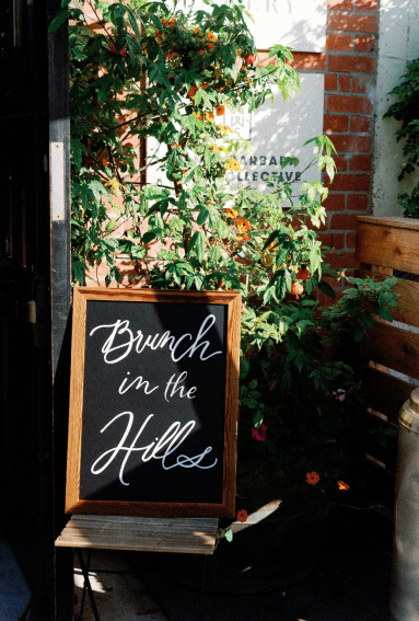 Handwritten brunch sign surrounded by greenery for a casual post-wedding gathering