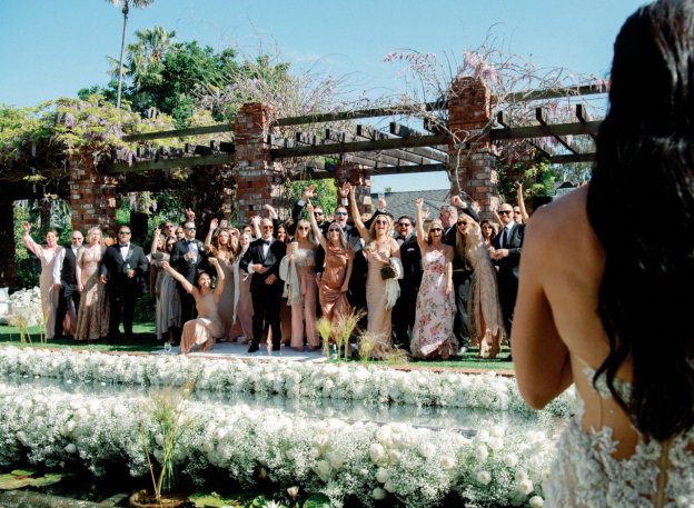 Bride facing a lively wedding party group posing for a celebration photo outdoors