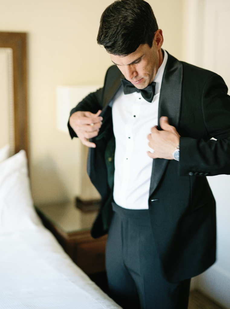 An image of a groom fixing his suit jacket