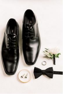 An image of a groom’s bow tie, shoes, cuff links, ring, and pocket flower 
