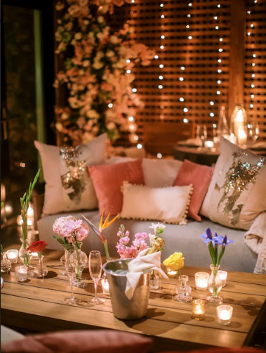 An image of floral arrangements and candles around a couch with fairy lights in the background