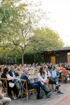 Wedding guests seated at an outdoor reception with string lights and rustic decor