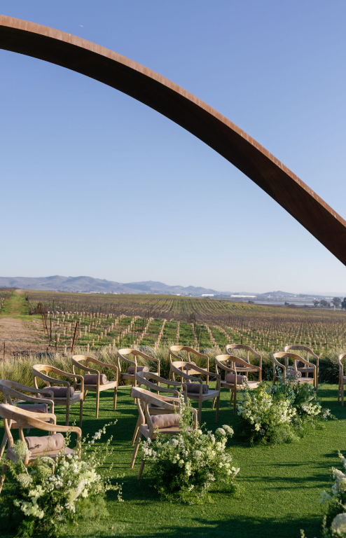 Outdoor vineyard wedding ceremony setup in Napa Valley with wooden chairs, greenery, and a panoramic view of the vine
