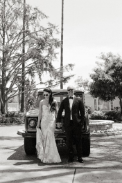 An image of a bride and groom posing in front of a car