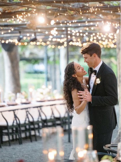 Couple dancing at their wedding with a beautifully decorated venue and twinkling fairy lights in the background.