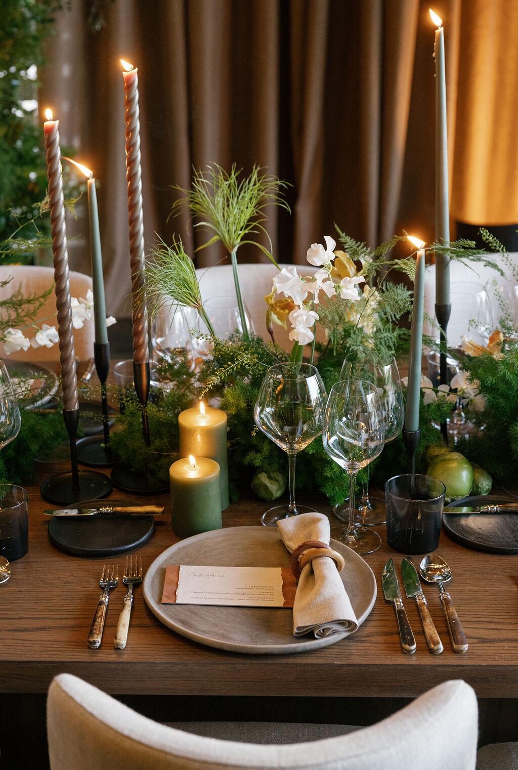 A close-up of a luxury tablescape setting featuring green florals, a personalized name card, and cutlery