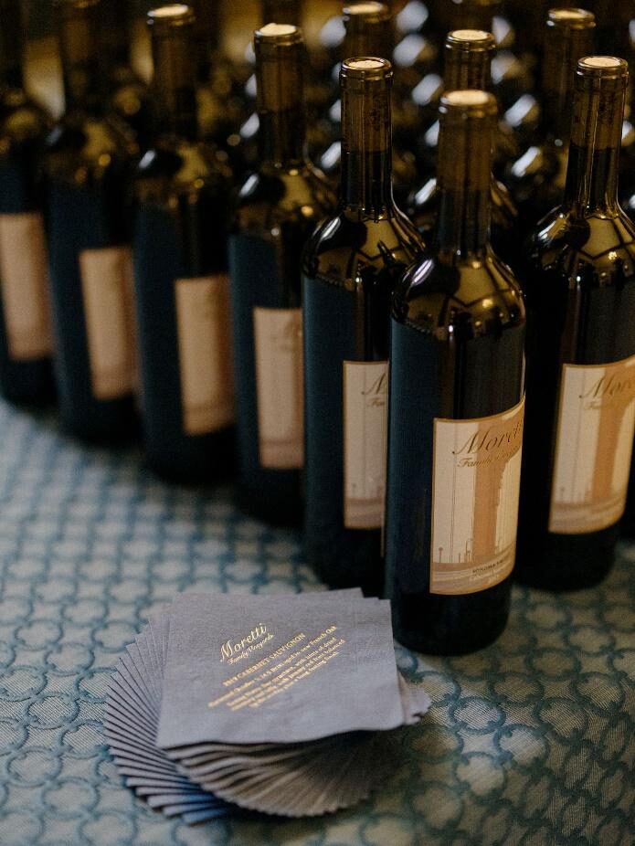 Close-up of wine bottles wrapped with personalized napkins, showcasing thoughtful custom details for a luxury wedding welcome event