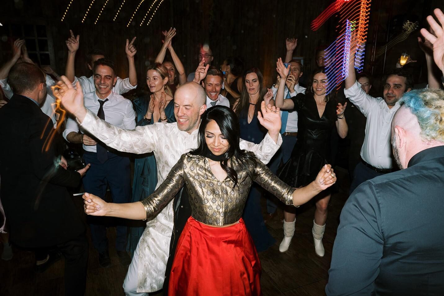 A high-energy photo of a bride and groom dancing joyfully in the center of a crowded dance floor surrounded by cheering guests