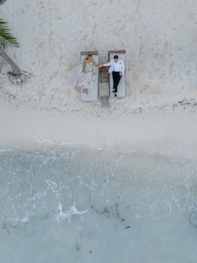 A couple holding hands while sitting on beach chairs, captured from above in a scenic beach setting in Mexico.