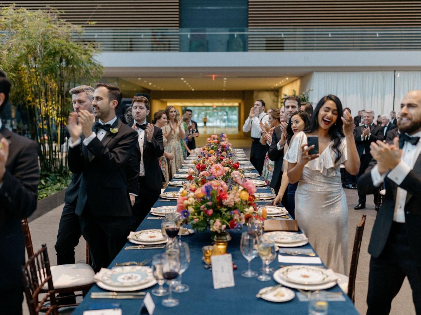 A wedding reception dinner in a museum setting, guests clapping for the bride and groom