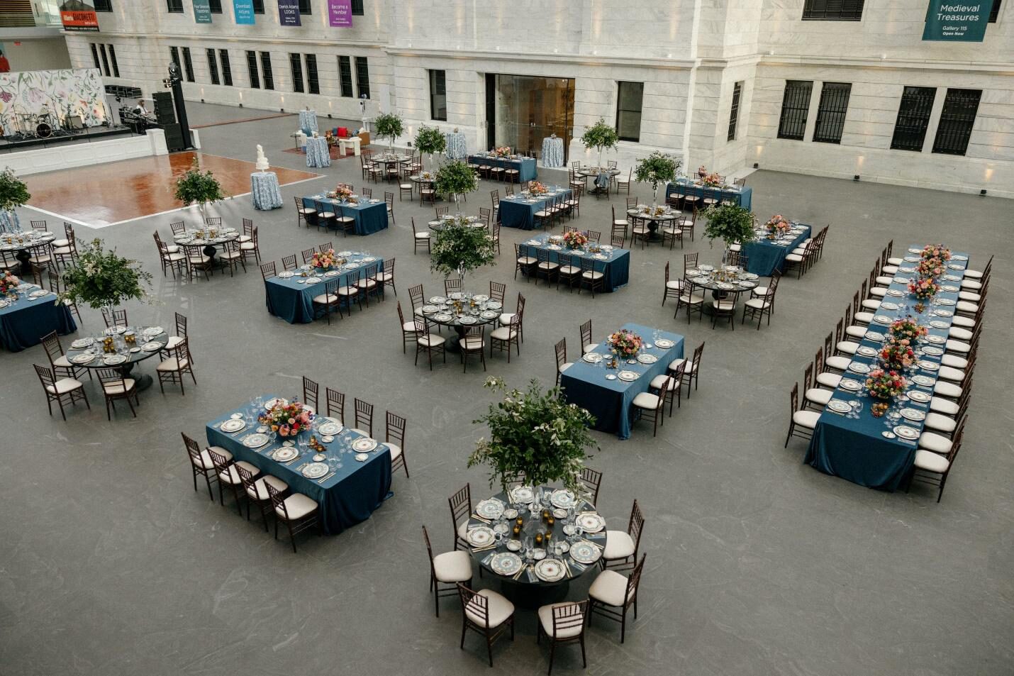 Aerial view of a museum's grand, marble hall set up for a wedding reception. Showing a mix of square and rectangular tables.
