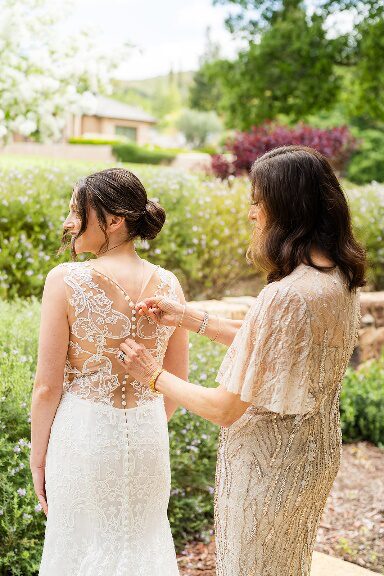 An image of a woman buttoning up a bride’s wedding dress